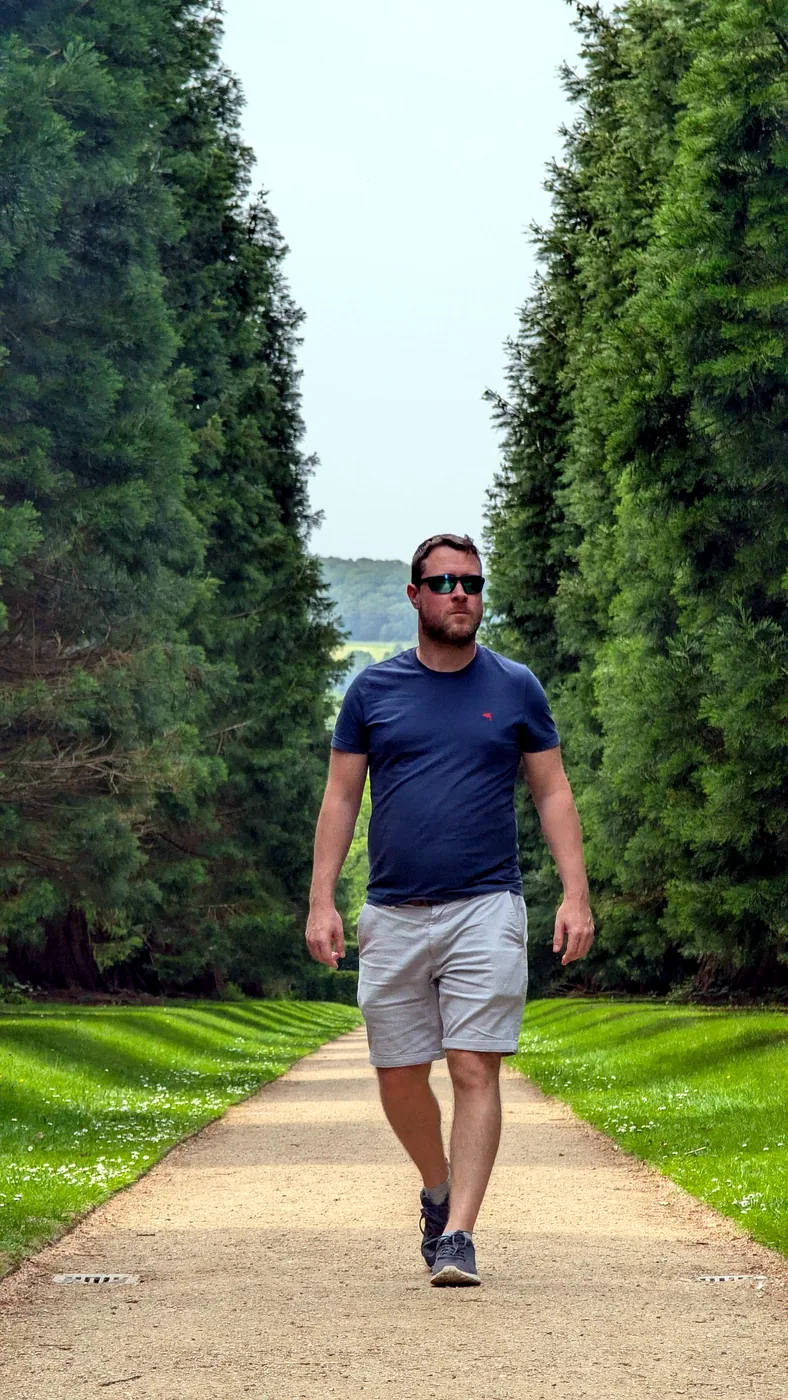 James walking down a long path between tall green trees
